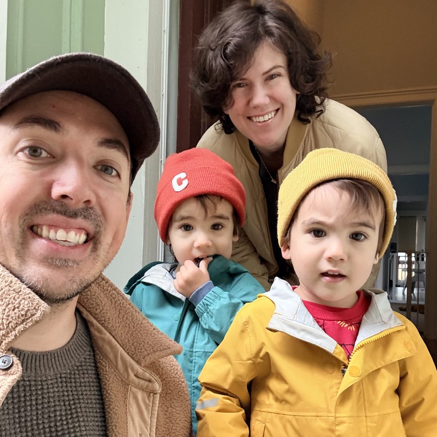 Selfie of James with his wife and two young sons in bright rain jackets and beanies at their front door